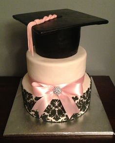 a cake with a graduation cap on top and pink ribbon around the edge, sitting on a table