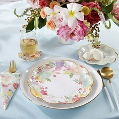 an arrangement of flowers in a vase on a table with plates and utensils