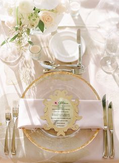 the table is set with white and gold plates, silverware, and napkins