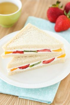 a white plate topped with a cut in half sandwich next to a cup of tea