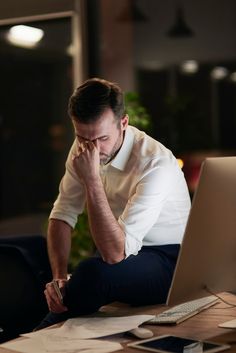 a man sitting in front of a laptop computer with his hand on his face while looking at the screen