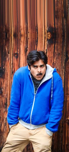 a man standing in front of a wooden wall wearing a blue jacket and khaki pants