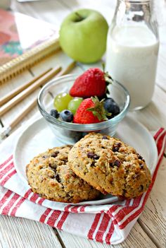 two oatmeal cookies on a plate with fruit and milk