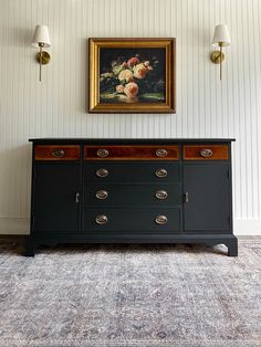 a painting hangs on the wall next to a black dresser with drawers and knobs