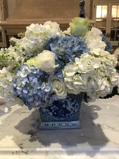 a blue vase filled with white flowers on top of a marble countertop next to a chandelier