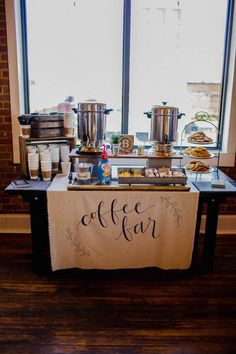 a buffet table with coffee and pastries on it in front of a large window