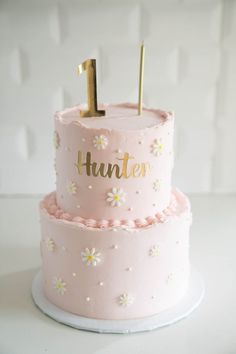 a pink cake with gold letters and flowers on it