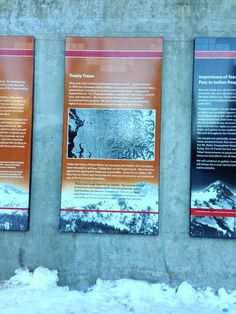 three signs on the side of a building with snow around them and mountains in the background