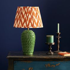 a green lamp sitting on top of a wooden table next to a candle and a book