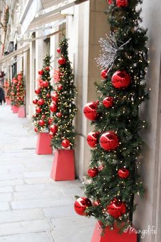 christmas trees lined up on the side of a building with red balls and ornaments hanging from them