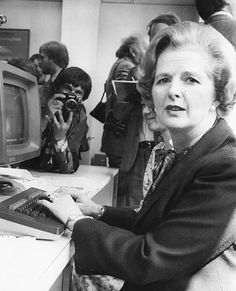 an older woman typing on a computer in front of a group of people with cameras