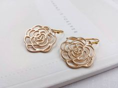 These are pair of beautiful camellia rose earrings. They are made with golden plated over brass flower shaped filigree pendants. The flower is available in two different golden color. The gold color is in a deep gold; and light gold color is in a light gold tone. The earrings measure about 31mm (1.25 inches) from the top of the ear wires to the bottom of the flower. They are perfect for many occasions, gift giving or as a little treat for yourself. Your earrings will presented in a jewelry gift Rose Gold Earrings With Rose Flower Design, Gold Rose Design Earrings For Wedding, Gold Rose Design Earrings For Anniversary, Gold Earrings With Rose Design For Gift, Gold Earrings With Rose Design As Gift, Formal Gold Earrings With Rose Design, Rose Gold Flower Earrings For Formal Occasions, Rose Gold Flower Earrings With Rose Design, Rose Gold Rose Design Flower Earrings For Formal Occasions