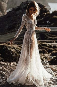 a woman in a long dress standing on rocks near the ocean with her arms outstretched