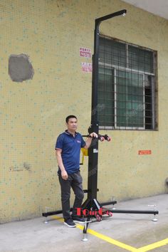 a man standing next to a pole with a machine in front of it on the side of a building