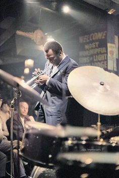 a man in a suit playing the trumpet on stage with other people sitting around him