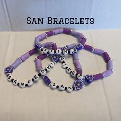 three purple and white bracelets with words written in small letters on them, sitting next to each other