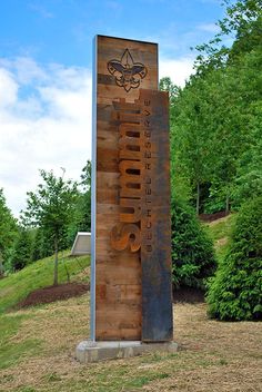 a large metal sign sitting on top of a lush green field next to trees and bushes