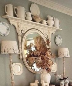 a white dresser topped with lots of dishes and vases next to a wall mounted mirror