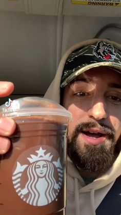 a man in a car holding up a cup of coffee with the starbucks logo on it