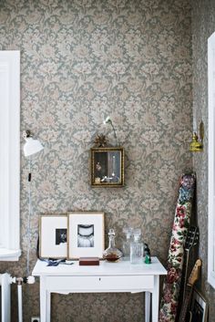 a small white table with two pictures on it in front of a floral wallpapered wall