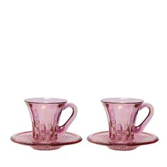 two pink glass cups and saucers sitting next to each other