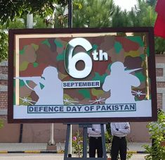 two men standing in front of a sign that says 6th september defence day of pakistan