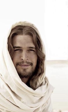 a man with long hair and beard wearing a white shawl over his head is smiling