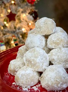 a pile of powdered sugar balls on a red plate next to a christmas tree