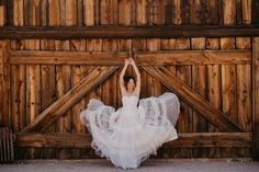 a woman standing in front of a wooden wall wearing a white dress and holding her arms up