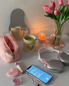 a white table topped with pink flowers and headphones next to a cell phone on top of it