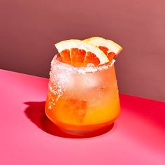 an orange drink is garnished with powdered sugar and slices of lemon on a pink surface