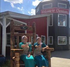 two women sitting on wooden chairs in front of a building