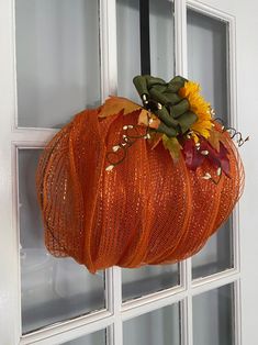 an orange mesh pumpkin with sunflowers and leaves hanging from it's side