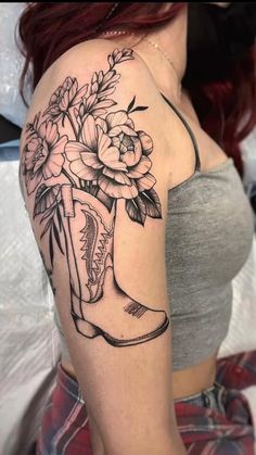 a woman's arm with flowers and boots tattooed on her left shoulder, while she is wearing a gray tank top