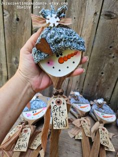 a hand holding a snowman ornament on top of a wooden pole with tags attached to it