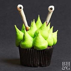 cupcakes decorated with green icing and googly eyes are displayed in front of a black background