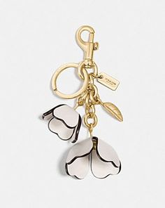 a keychain with three white flowers hanging from it's center, on a gold chain