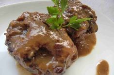 two pieces of meat covered in gravy on a white plate