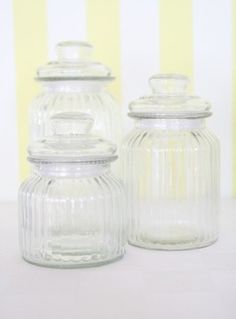 three clear glass jars with lids on a white tableclothed wall behind them are yellow striped walls