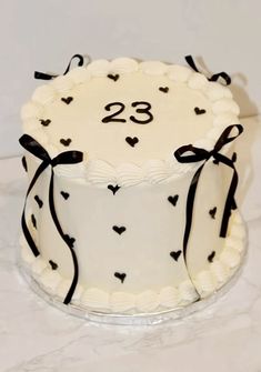 a white cake decorated with black hearts and ribbon on a marble countertop in front of a white wall