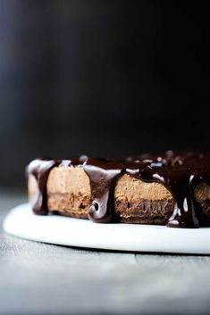 a piece of cake with chocolate icing on a white plate, sitting on a table