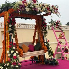 an outdoor seating area with flowers and greenery on the top, next to a pink ladder