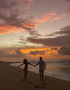 two people holding hands walking on the beach at sunset with footprints in the sand as the sun sets