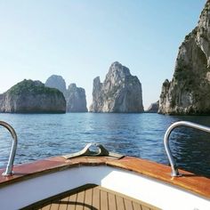 the bow of a boat traveling through an ocean with rock formations in the background and blue sky