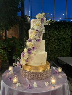 a three tiered wedding cake with purple and white flowers on the top is surrounded by candles