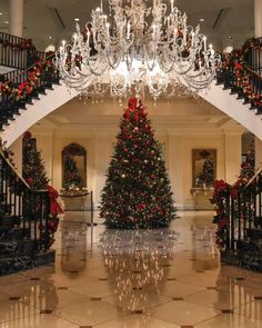 a christmas tree is in the middle of a foyer with chandelier and stairs