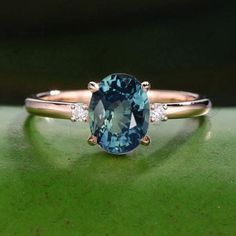 an oval blue and white diamond ring sitting on top of a green surface