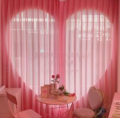 a pink room with sheer curtains and a round table in the corner, along with two chairs