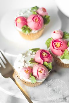 three cupcakes decorated with pink flowers and green leaves are on a white plate