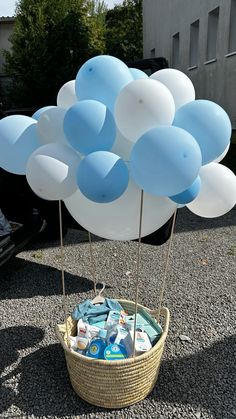 a basket filled with blue and white balloons sitting on top of a gravel road next to a building